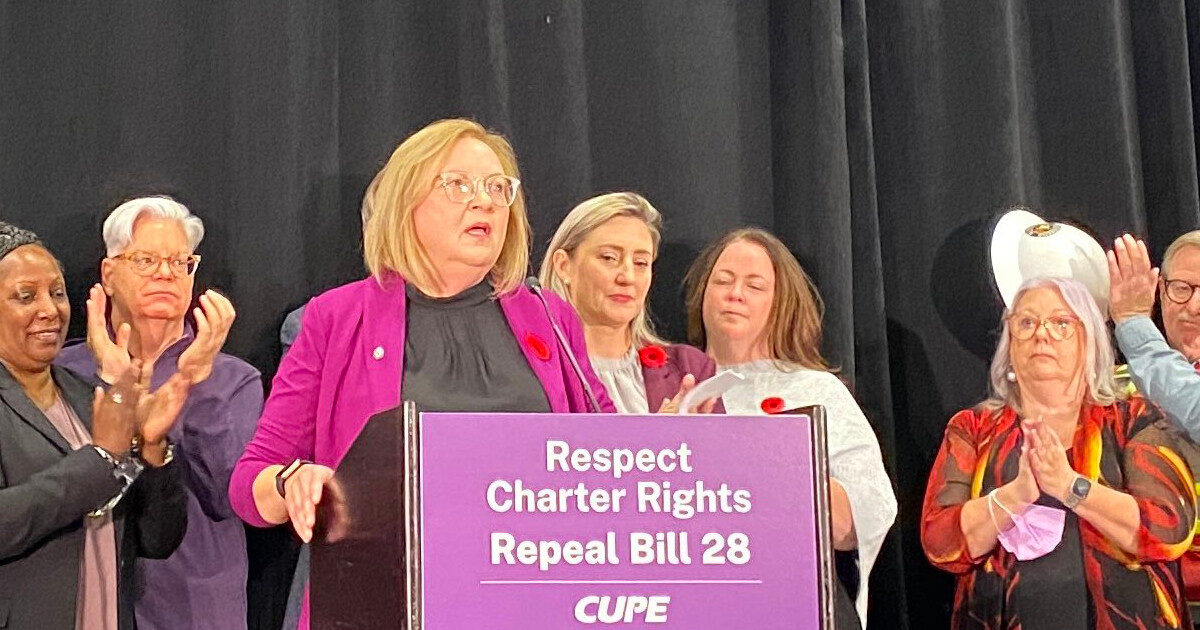 Unifor National President Lana Payne at a CUPE press conference with placard reading Respect Charter Rights Repeat Bill 28